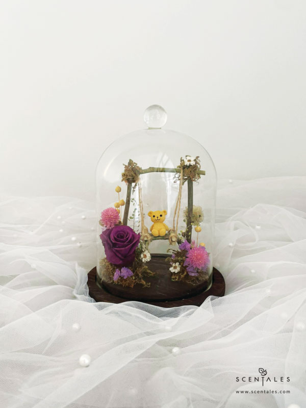 Dried and Preserved bell jar with Bear, swing, preserved dark purple rose, dried pink gomphrena, dried brown scabiosa stellata, ixodia, lilac statice, dried thlaspi, plenty of dried lino and moss