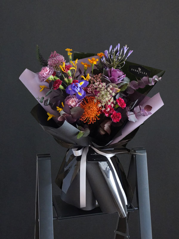 Midnight Masquerade Flower Bouquet Fresh flower bouquet with Nile Lily, blue iris, purple brassica, orange leucospernum, gradient purple carnation, dark purple spray carnation, dark purple pompom, orange marigold tagetes, pink rice flower, mini allium, yellow kangaroo paw, dark purple ammi, fox tail and plenty of eucalytus