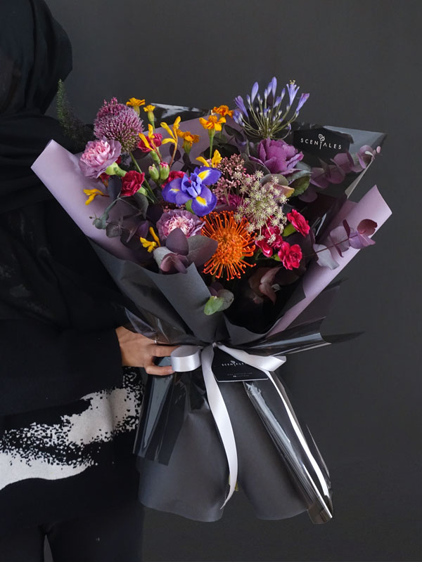 Midnight Masquerade Flower Bouquet Fresh flower bouquet with Nile Lily, blue iris, purple brassica, orange leucospernum, gradient purple carnation, dark purple spray carnation, dark purple pompom, orange marigold tagetes, pink rice flower, mini allium, yellow kangaroo paw, dark purple ammi, fox tail and plenty of eucalytus